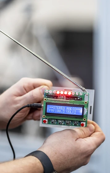 Close-up of a small electronic device with an LCD screen displaying radio frequency settings, held by a person in a technical lab. Close-up of a small electronic device with an LCD screen displaying radio frequency settings, held by a person in a technical lab.